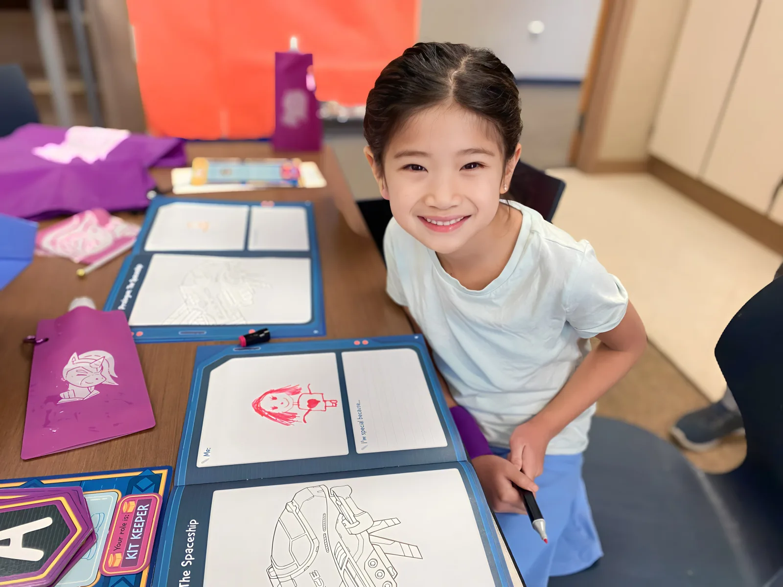 Smiling girl showing a workbook reflection page at her desk